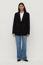 Person wearing a black blazer and blue jeans on a white background