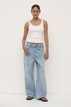 Woman wearing a white tank top and light blue jeans on a white background