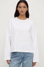 Person wearing a white long-sleeve shirt and light blue jeans on a plain background