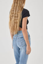 Person wearing a black crop top and light blue jeans on a plain background