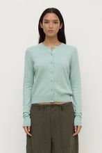 Woman wearing a light blue cardigan and green pants on a white background
