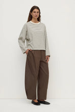 Woman wearing a light gray sweater and brown pants on a white background