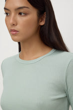 Woman wearing a light green ribbed long-sleeve top against a white background