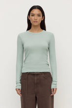Woman wearing a light green long-sleeve top and brown pants on a white background