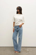 Person wearing a white top and blue jeans against a plain background