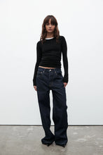 Person wearing a black long-sleeve top and dark jeans against a white background