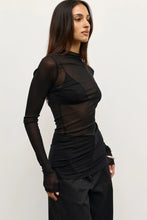 Woman wearing a black outfit with sheer sleeves on a white background