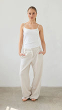 Woman wearing a white top and beige pants against a plain background