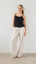 Woman wearing a black tank top and beige wide-leg pants against a plain background
