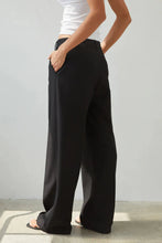Person wearing black wide-leg pants and a white top against a plain background