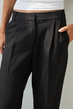 Black pleated pants worn by a person on a neutral background