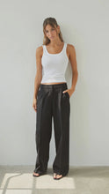 Woman wearing a white tank top and black wide-leg pants against a plain background