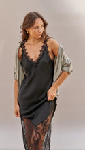 Woman wearing a black slip dress with lace details and an olive green cardigan on a neutral background