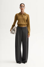 Woman wearing a mustard yellow top and dark gray pants on a white background