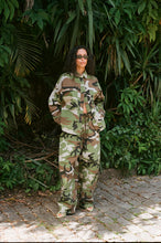 Person wearing a camouflage outfit standing in front of green foliage.