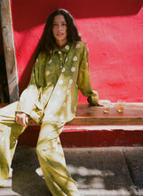 Woman in a green and white polka dot outfit sitting at a wooden table against a red wall.
