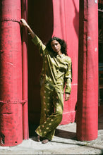 Woman in a green polka dot outfit standing against red columns.