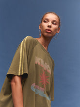 Person wearing a green oversized t-shirt with colorful text and graphics against a blue background