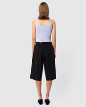 Woman wearing a light blue tank top and black high-waisted shorts on a white background