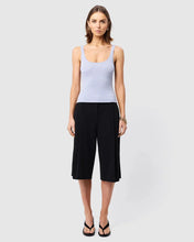 Woman wearing a light purple tank top and black capri pants on a white background