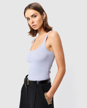 Woman wearing a light blue ribbed tank top and black pants on a plain background