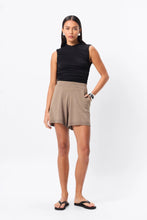 Woman wearing a black sleeveless top and beige skirt on a white background