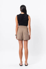 Person wearing a black sleeveless top and beige shorts on a white background