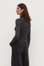 Woman wearing a dark gray long-sleeve top and black pants on a white background