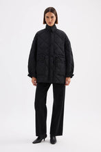 Person wearing a black quilted jacket and pants on a white background