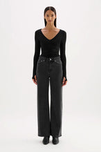 Woman wearing a black long-sleeve top and black high-waisted jeans on a white background