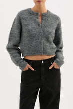 Person wearing a gray knitted cardigan and black pants on a white background