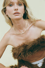 Woman wearing a fur stole and gold necklace against a plain background