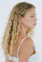 Woman with long, wavy blonde hair wearing a white polka dot dress against a white background