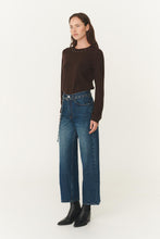 Woman wearing a brown long-sleeve top and blue jeans on a white background