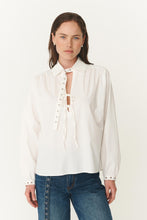 Woman wearing a white blouse with a tie detail and blue jeans on a white background