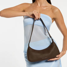 Woman carrying a brown shoulder bag on a plain background